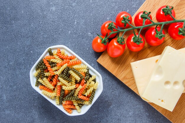 Alguma massa colorida com tomates, queijo do macarrão em uma bacia na superfície cinzenta, vista superior.