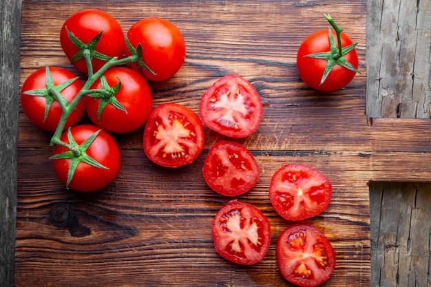 Alguns tomates e fatias com faca em uma vista superior de tábua de madeira.