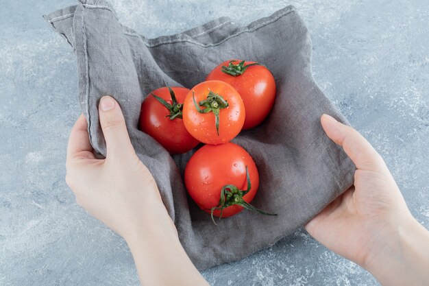 Alguns tomates frescos em uma toalha de mesa cinza.