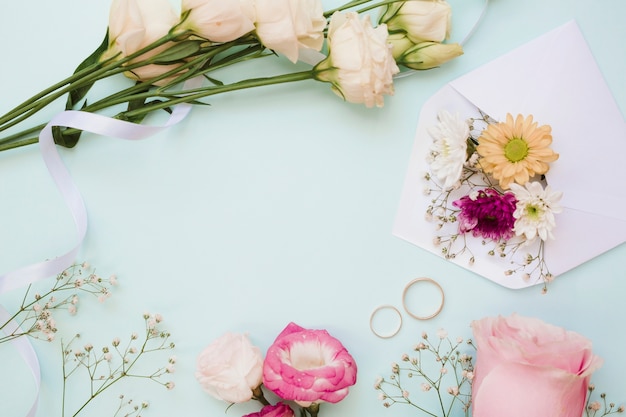 Alianças de casamento e decoração de flores sobre fundo azul pastel