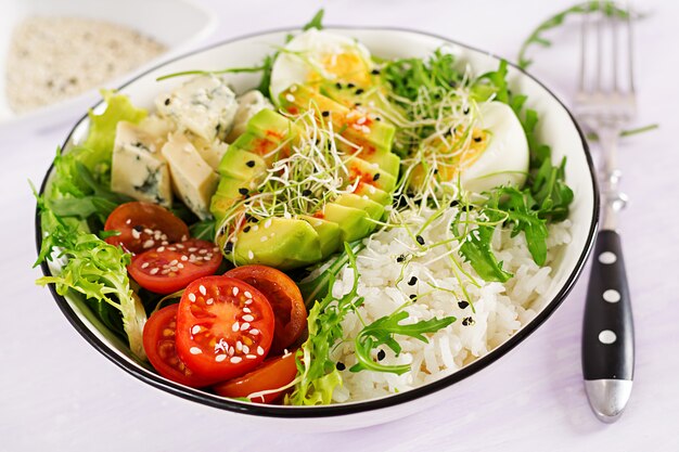 Alimento verde saudável da bacia de buddha do vegetariano com ovos, arroz, tomate, abacate e queijo azul na tabela.