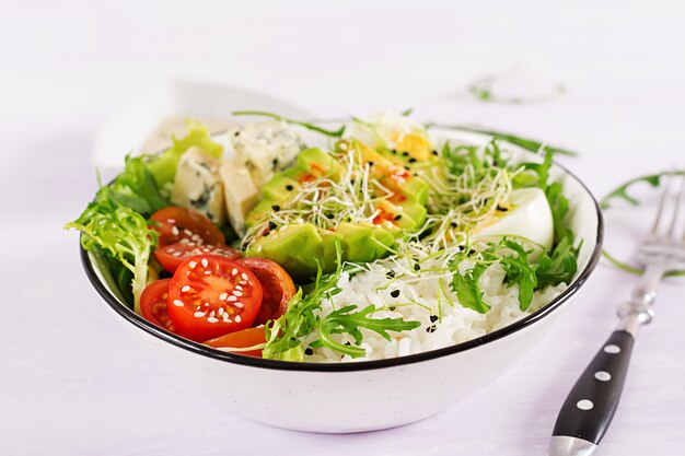 Alimento verde saudável da bacia de buddha do vegetariano com ovos, arroz, tomate, abacate e queijo azul na tabela.