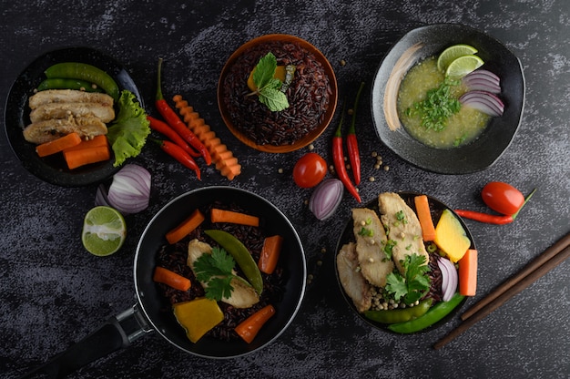 Alimentos variados e pratos de legumes, carne e peixe em uma mesa de pedra preta. Vista do topo.