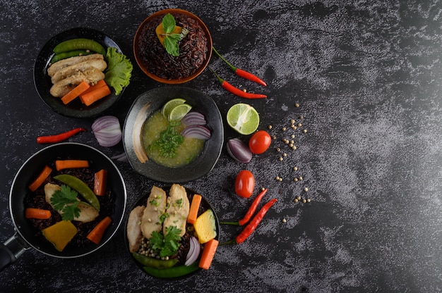 Alimentos variados e pratos de legumes, carne e peixe em uma mesa de pedra preta. Vista do topo.