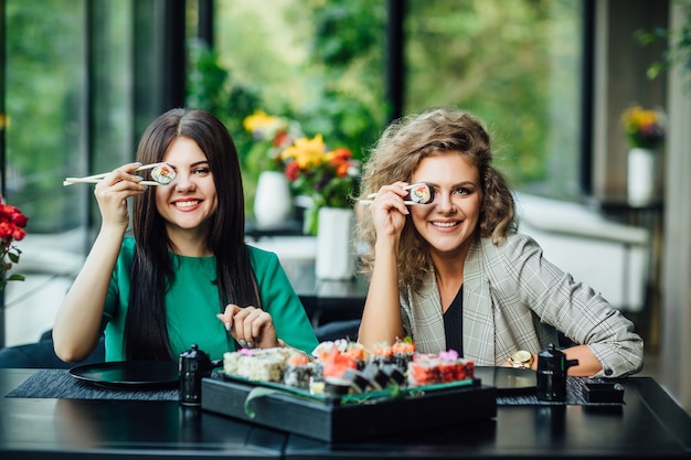 Foto grátis almoço em restaurante chinês na esplanada. duas irmãs comem sushi com palitos chineses.