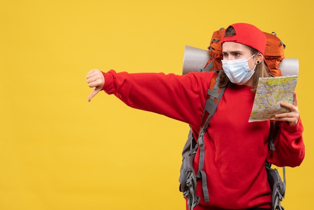 Alpinista feminina de vista frontal com mochila e máscara segurando o mapa dando o polegar para baixo