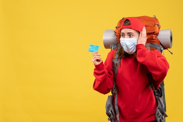 Alpinista perplexa com uma mochila e uma máscara segurando um cartão de crédito de frente