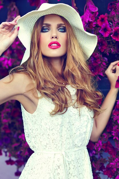 Alta moda look.glamor closeup retrato do modelo sexy elegante loira jovem bonita com maquiagem brilhante e lábios cor de rosa com perfeita pele limpa no chapéu perto de flores do verão