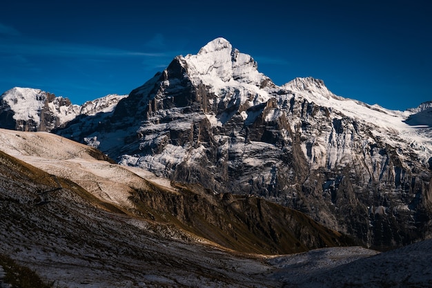 Altas montanhas rochosas cobertas de neve sob um céu azul claro na Suíça