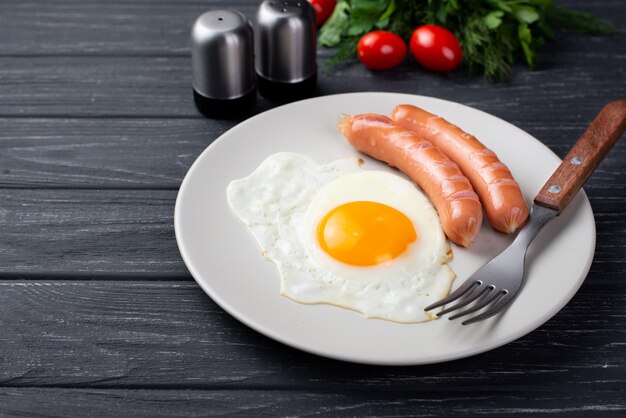 Alto ângulo de café da manhã ovo e salsichas no prato com tomates e ervas