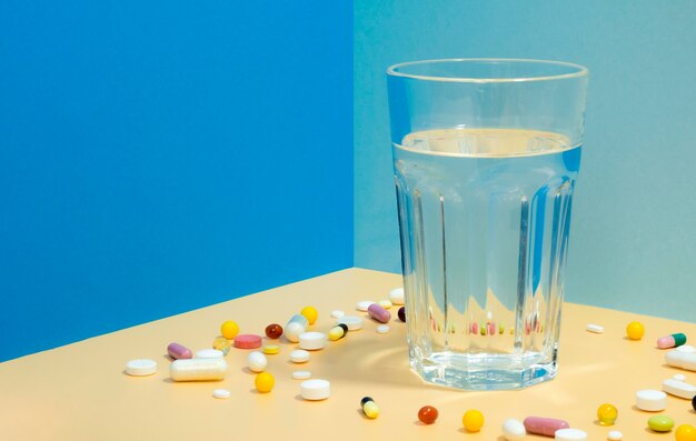Alto ângulo de copo de água com pílulas ao seu redor