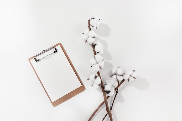 Alto ângulo de flores de algodão e um papel em branco em uma superfície branca