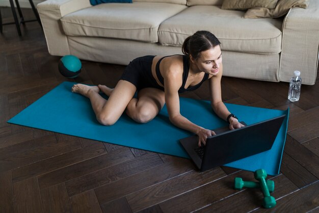 Alto ângulo de mulher com laptop no tapete de ioga