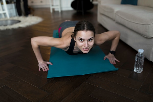 Alto ângulo de mulher fazendo yoga na esteira com garrafa de água