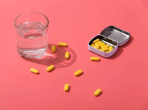 Alto ângulo de pílulas em recipiente de metal com copo de água