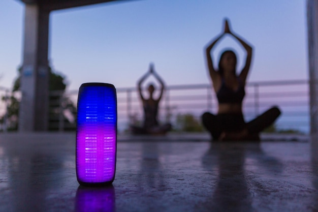 Alto-falante sem fio de luz de fundo colorido em primeiro plano da companhia de amigos fazendo ioga ouvindo música ao entardecer
