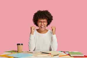 Foto grátis aluna alegre positiva posando na mesa contra a parede rosa