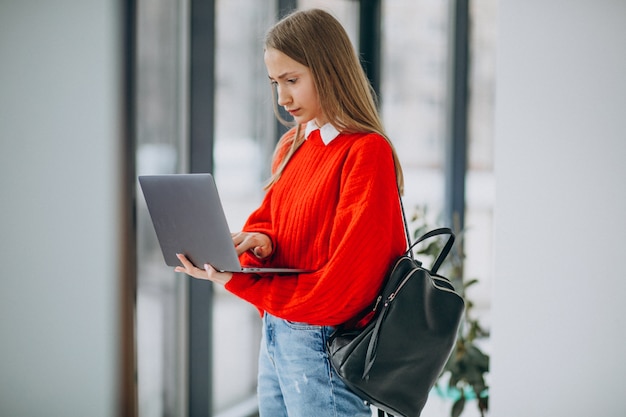 Aluna com laptop em pé junto à janela no corredor