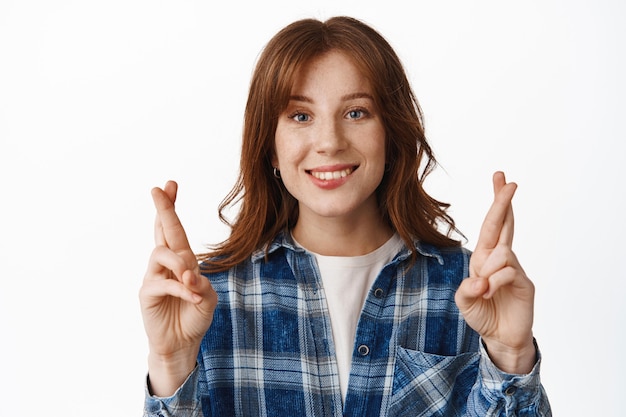 Foto grátis aluna esperançosa com cabelo ruivo e sardas, sorrindo feliz e fazendo um desejo em branco