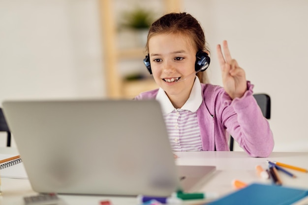 Aluna feliz levantando o braço para responder a pergunta enquanto tem aula on-line em casa