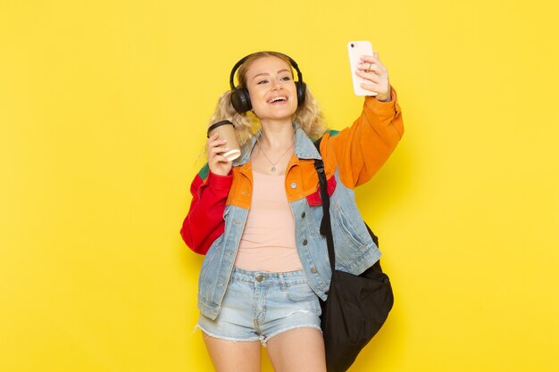 aluna jovem com roupas modernas tirando uma selfie em amarelo
