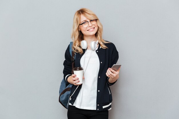 Aluna sorridente segurando a xícara de café e smartphone