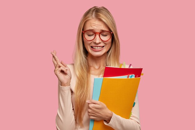 Aluna universitária loira estressante e preocupada posando contra a parede rosa