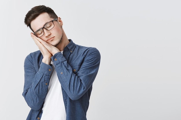 Aluno cansado de óculos apoiado nas palmas das mãos com os olhos fechados, dormindo