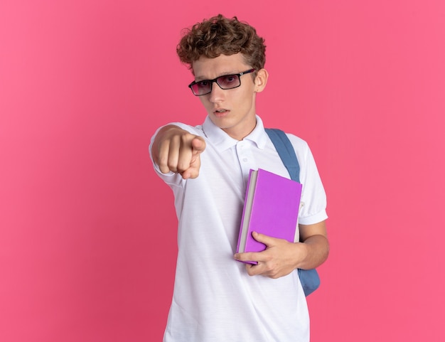Foto grátis aluno com roupas casuais usando óculos e mochila segurando o caderno apontando