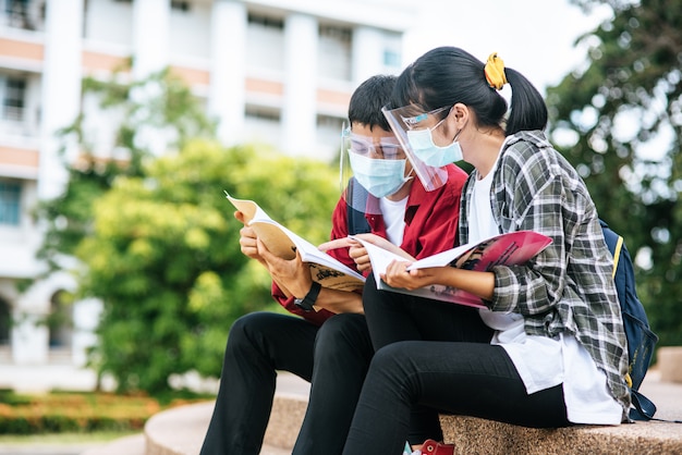 Alunos masculinos e femininos usando máscaras sentam e leem livros nas escadas