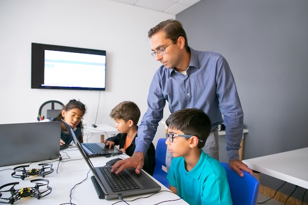 Alunos realizando tarefas em laptops e um professor focado monitorando-os