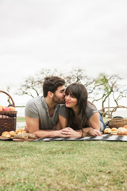 Amando o jovem casal deitado no tapete com comida assada e frutas no parque