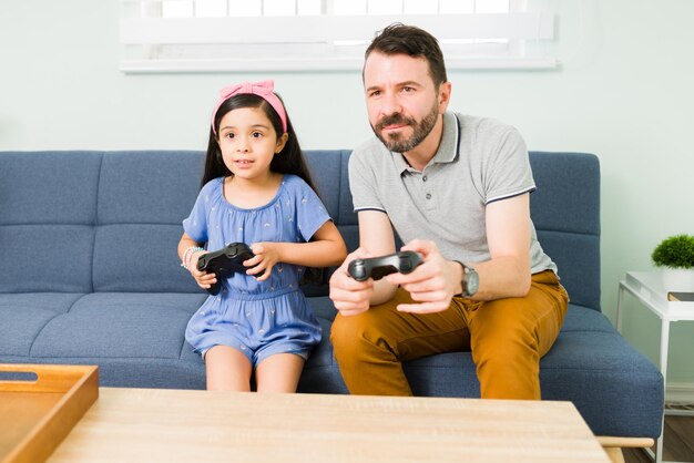 Amando o pai hispânico jogando videogame com sua filha fofa. Pai bonito, desfrutando de um dia divertido com sua filhinha