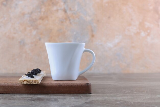 Ameixa seca fatiada no pão crocante e xícara de chá na tábua de madeira, na superfície de mármore