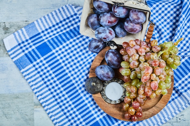 Ameixas frescas e um cacho de uvas na toalha de mesa.