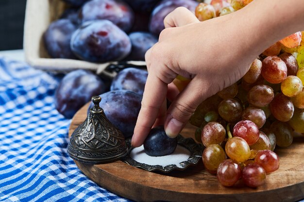 Ameixas frescas, um cacho de uvas e sal na placa de madeira.