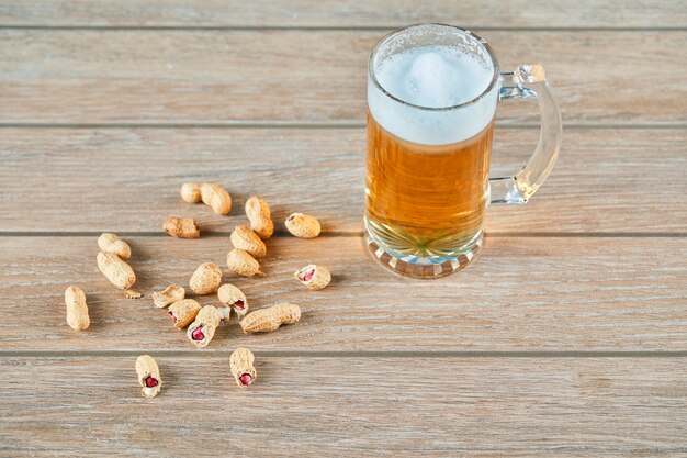 Amendoim e um copo de cerveja na mesa de madeira.