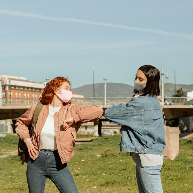 Amigas com máscaras ao ar livre fazendo saudação de cotovelo