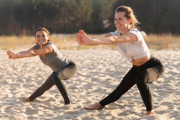 Amigas sorridentes fazendo exercícios na praia