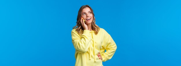 Amigável e despreocupada mulher loira falando ao telefone segurando o celular perto da orelha e olhando para cima