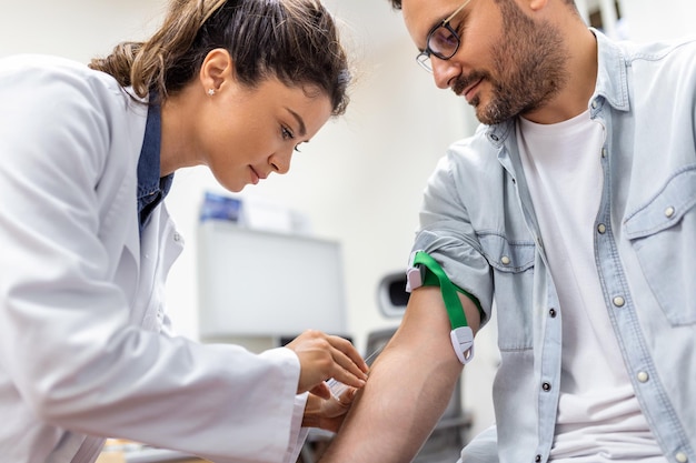 Amigável flebotomista do hospital coletando amostra de sangue do paciente no laboratório Preparação para exame de sangue pelo uniforme médico feminino na mesa na sala branca brilhante