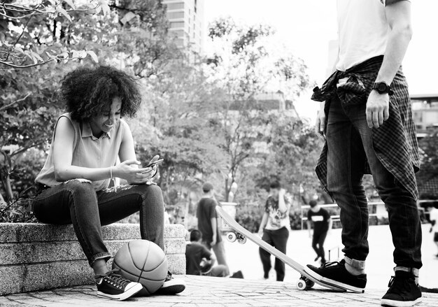 Amigos adultos jovens relaxando no parque usando smartphones e skate