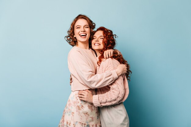 Amigos alegres, abraçando-se sobre fundo azul. Garotas animadas sorrindo e expressando boas emoções.