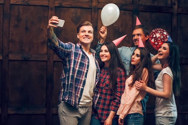 Foto grátis amigos alegres fazem selfie de aniversário. homem bonito com uma tatuagem segura um telefone para fazer selfie de si mesmo e seus amigos em sua festa de aniversário