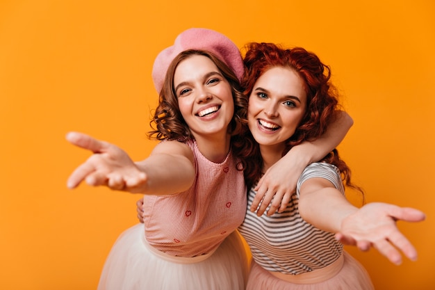 Amigos alegres se abraçando com um sorriso. Foto de estúdio de sorrir garotas atraentes posando em fundo amarelo.