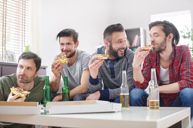 Amigos assistindo tv e comendo pizza