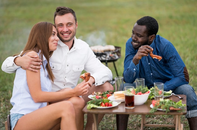 Amigos comendo ao lado de churrasco ao ar livre