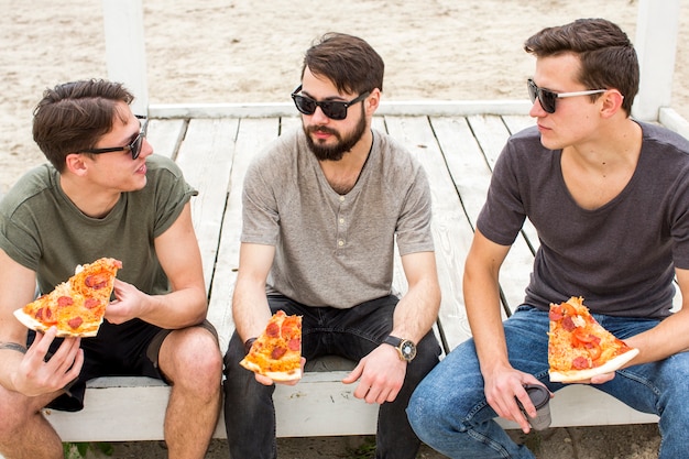 Amigos conversando enquanto está sentado com pizza na praia