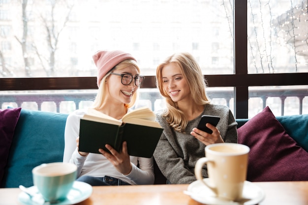 Amigos de duas mulheres felizes sentado no café e lendo o livro Foto gratuita