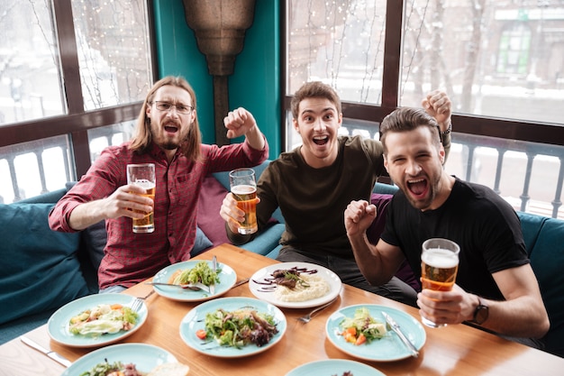 Amigos de homens alegres sentado no café enquanto bebia cerveja.